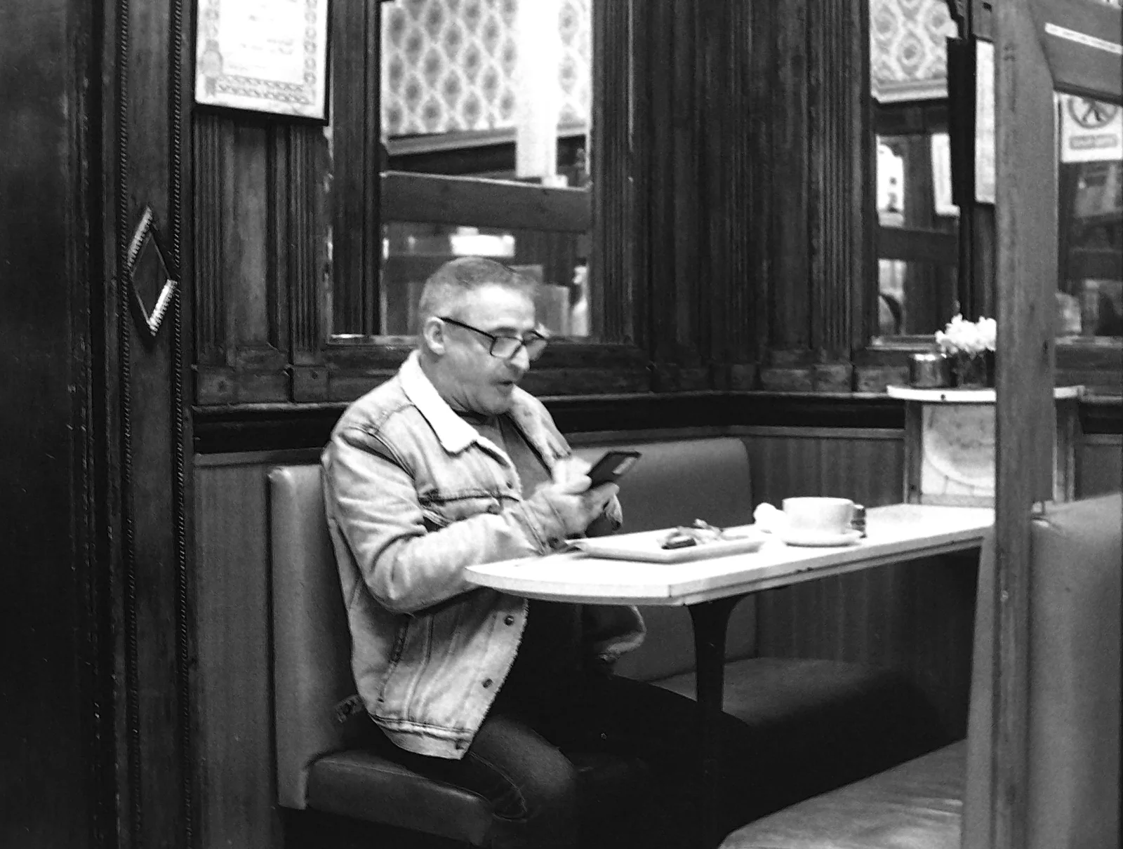 A man sits alone at a café table looking at his phone.