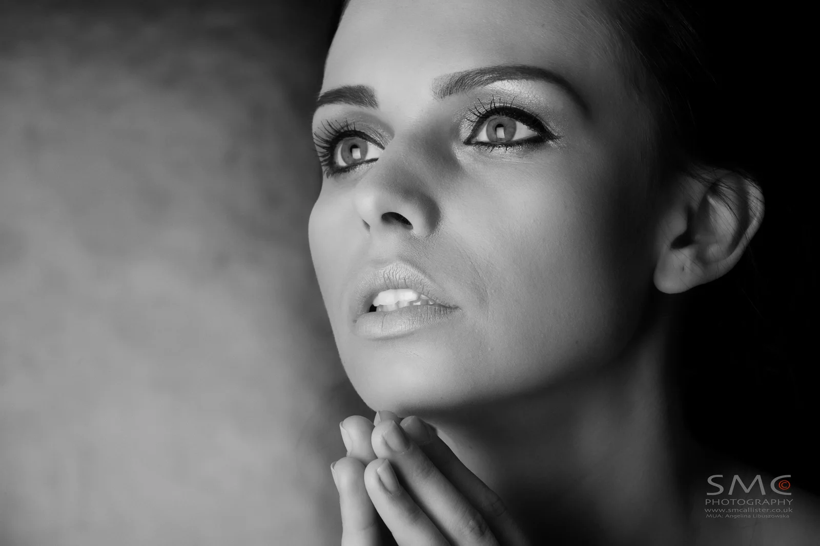 A woman looks upward with one hand resting lightly at her throat.