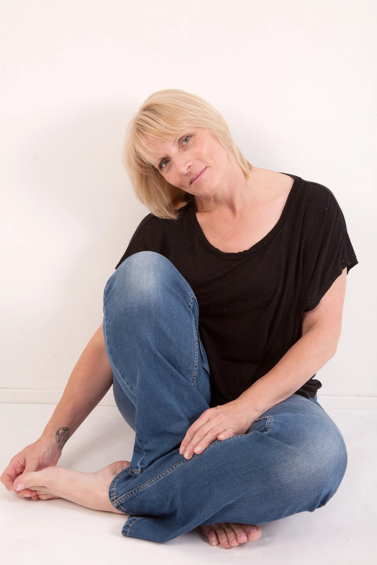 A woman sits casually against a pale background with one knee raised.