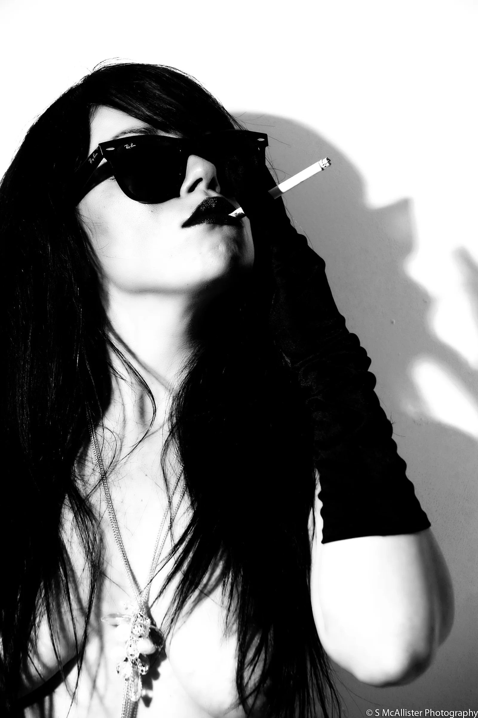 A woman in dark glasses holds a cigarette in a stark monochrome portrait.