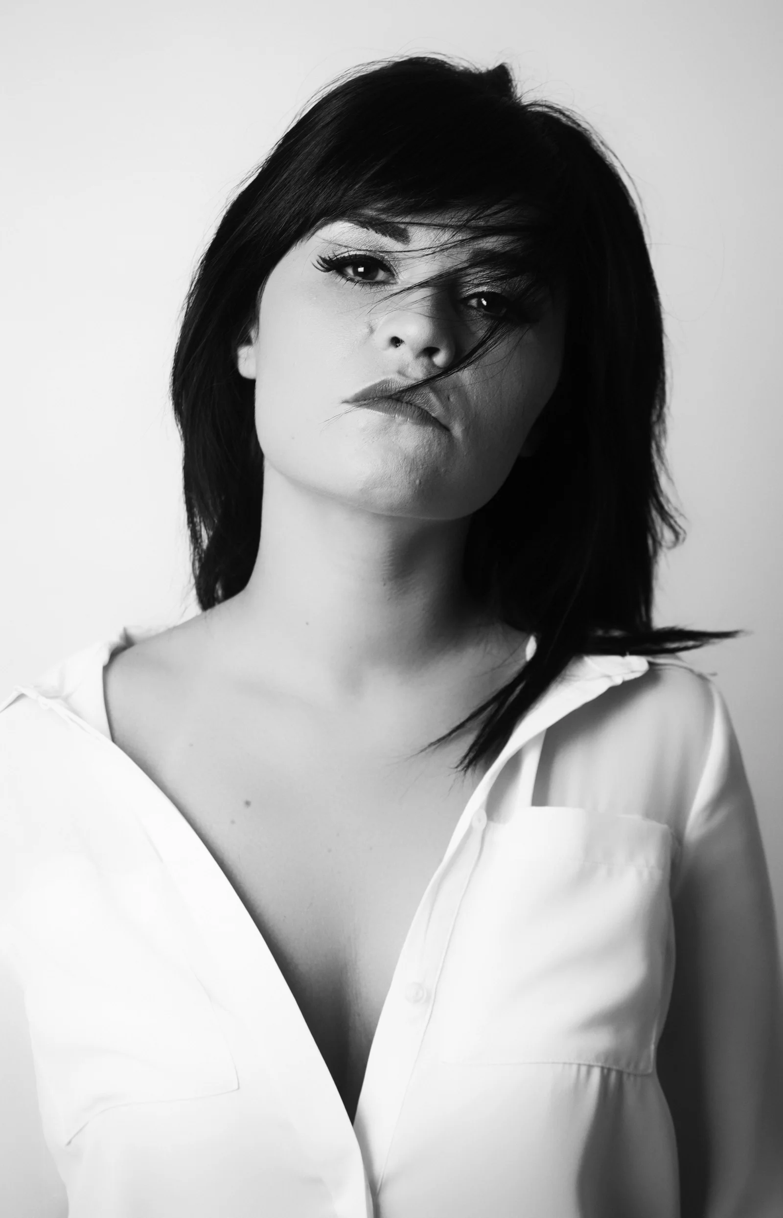 A woman in a white shirt looks forward as strands of hair cross her face.