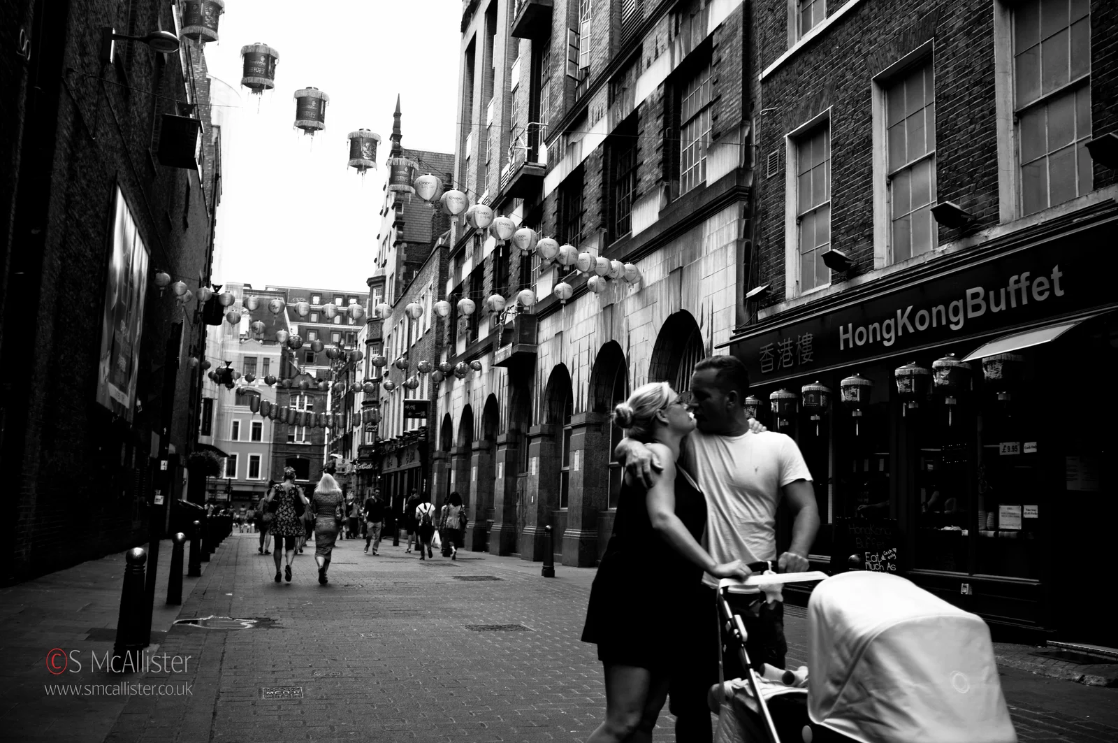 People move along a narrow city street between tall buildings.