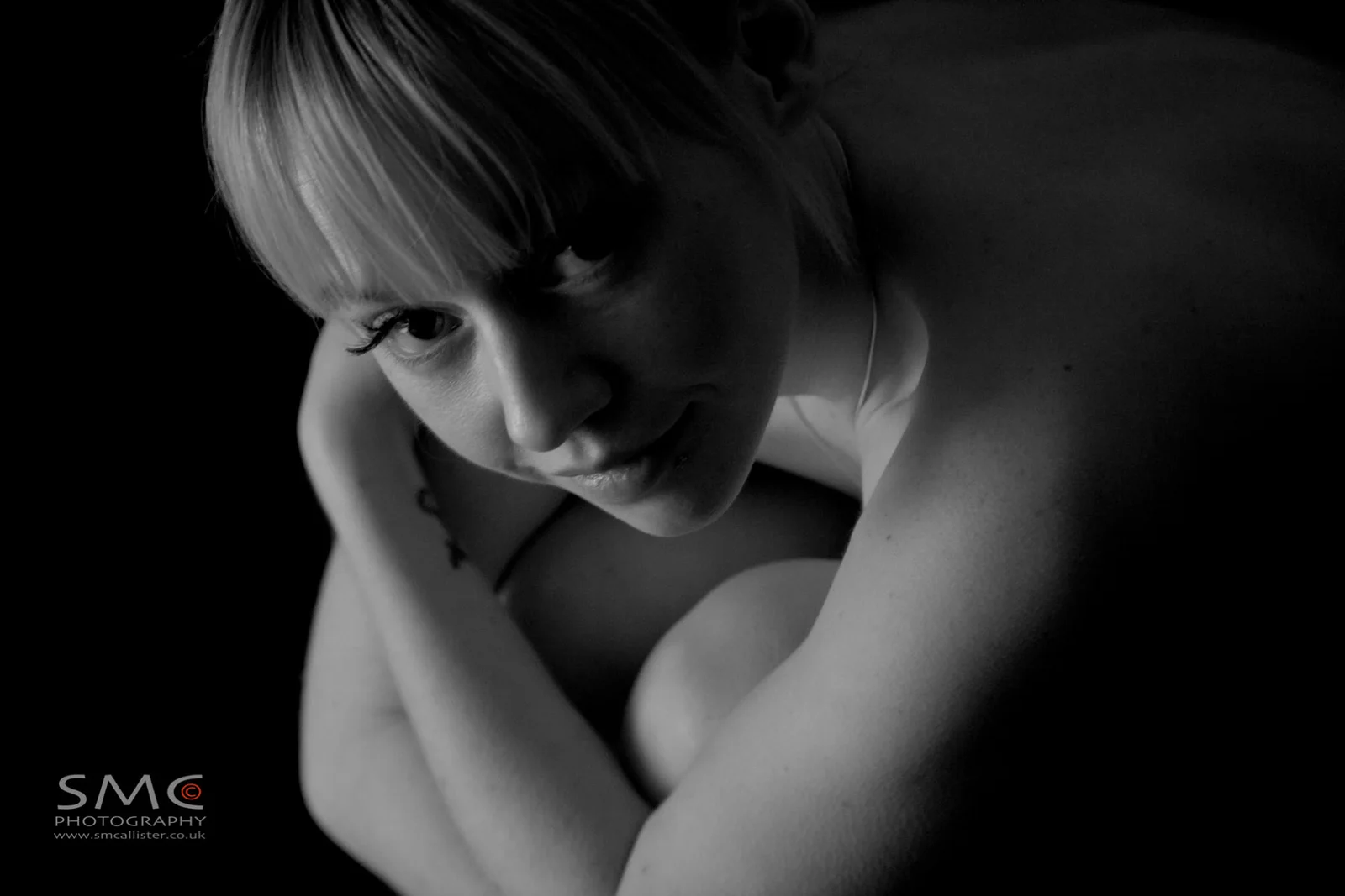 A woman curls inward in a low-key monochrome portrait.